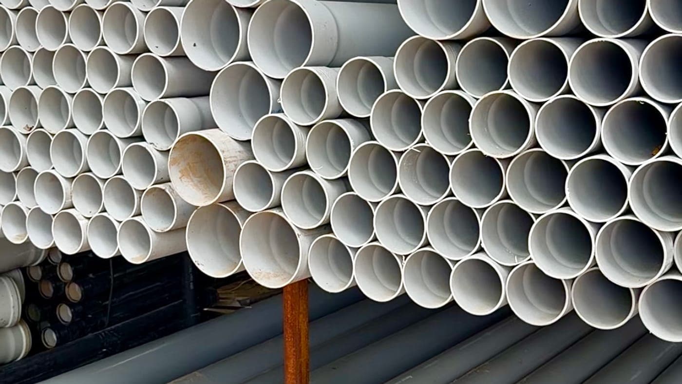 Stacks of white PVC pipes in several sizes on a rack in the yard